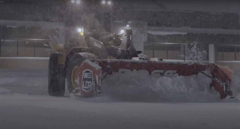 Snow plow clearing snow during winter storm in an urban area, ensuring safe roads and travel conditions.